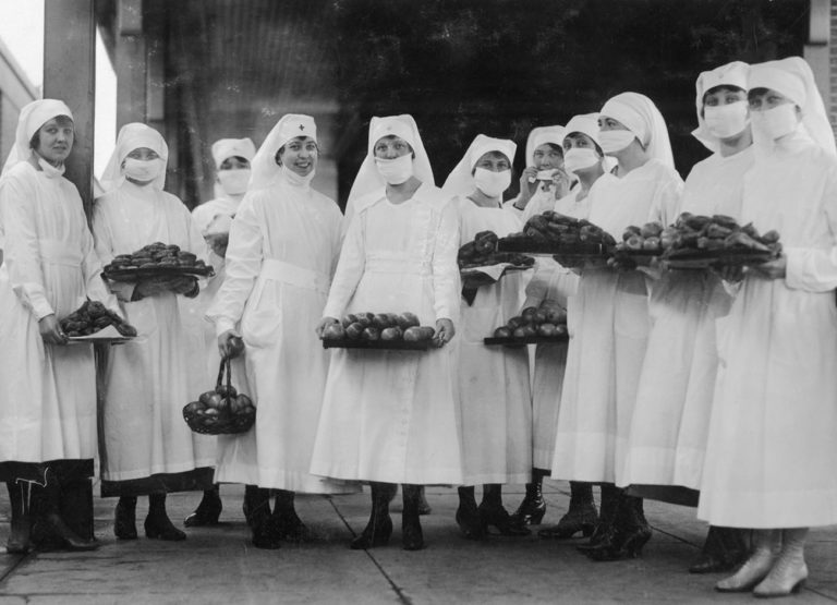 WWI nurses wear masks and hold plates of food for the sick.