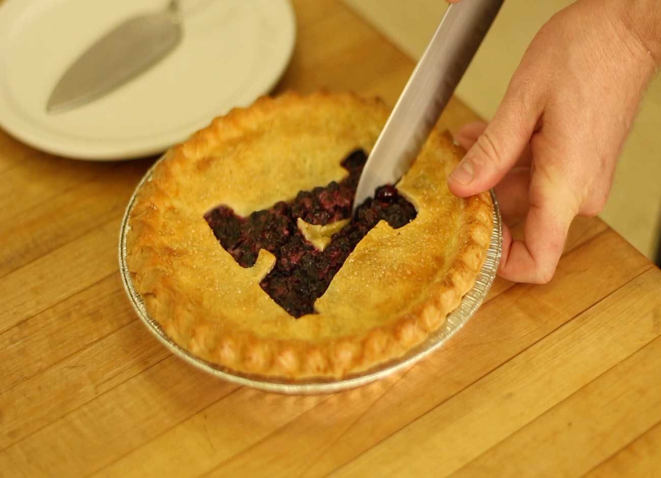 blueberry pie with person cutting an A into top crust