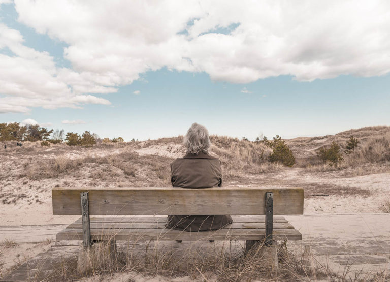older woman sitting on a bench looking at the sky