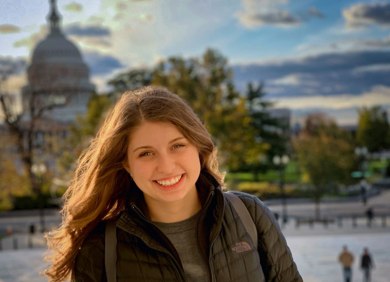 a young woman smiles while standing in front of the U.S. capitol building