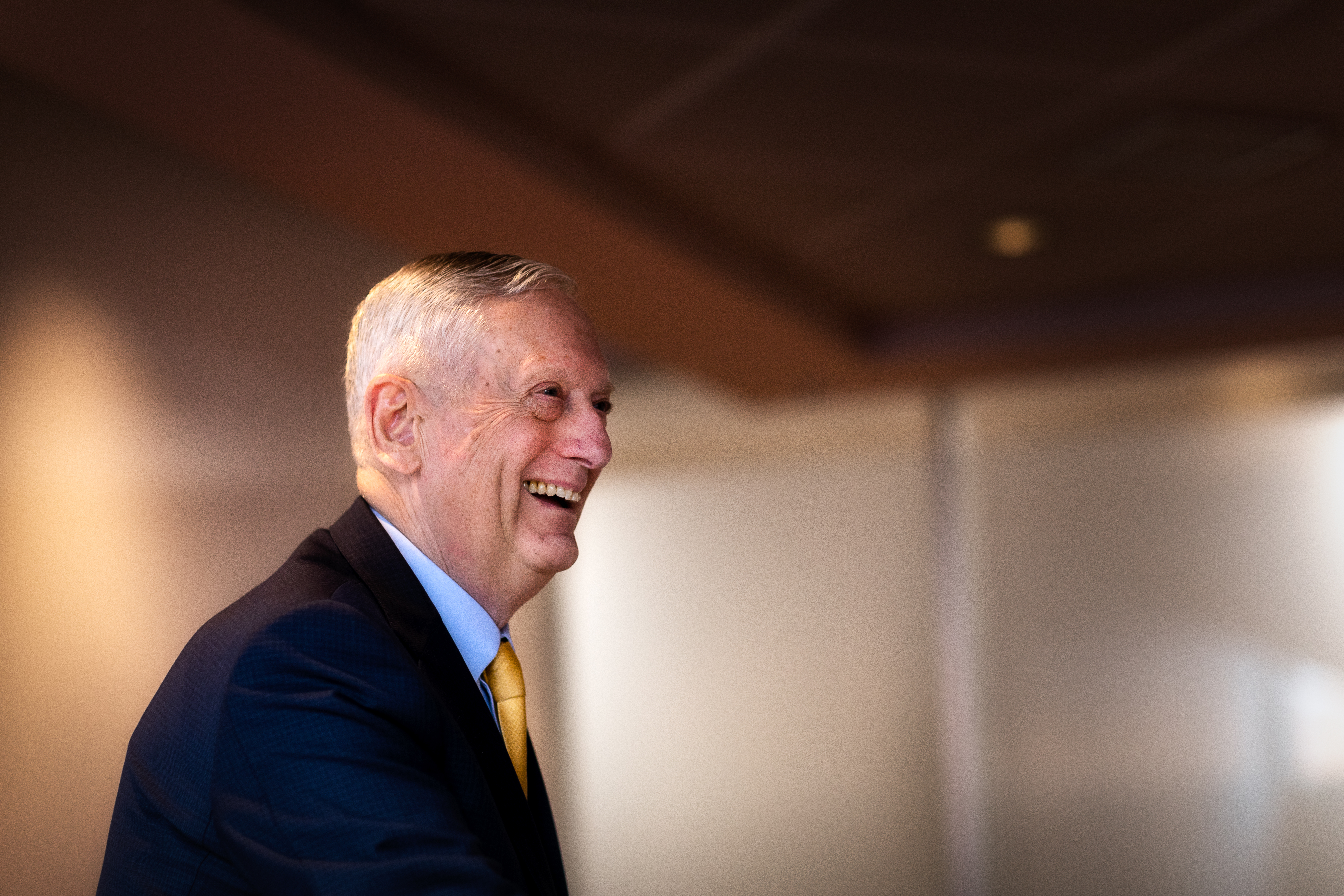 Jim Mattis smiles. He is wearing a suit and yellow tie.