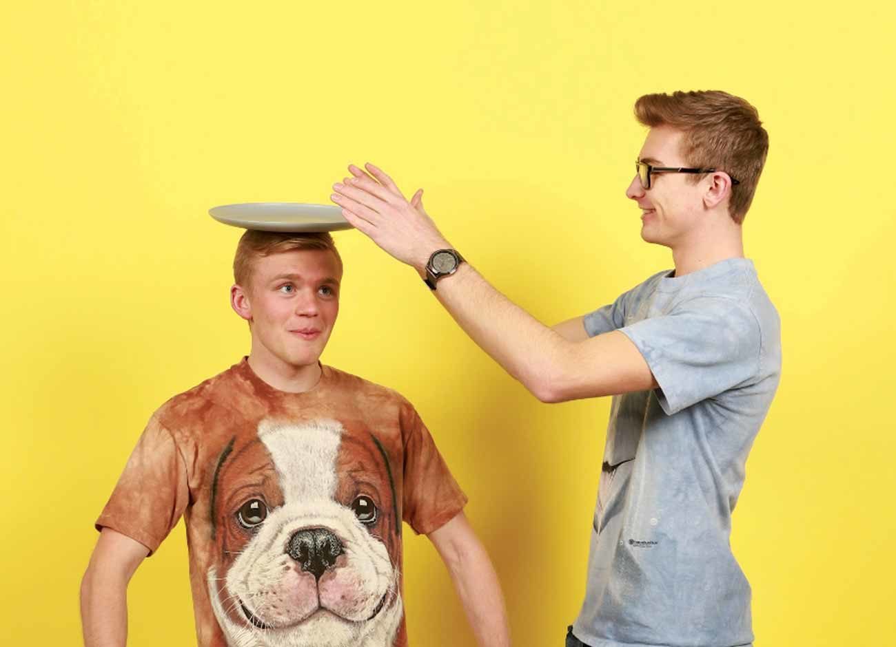 a young man balances a plate on the head of his friend
