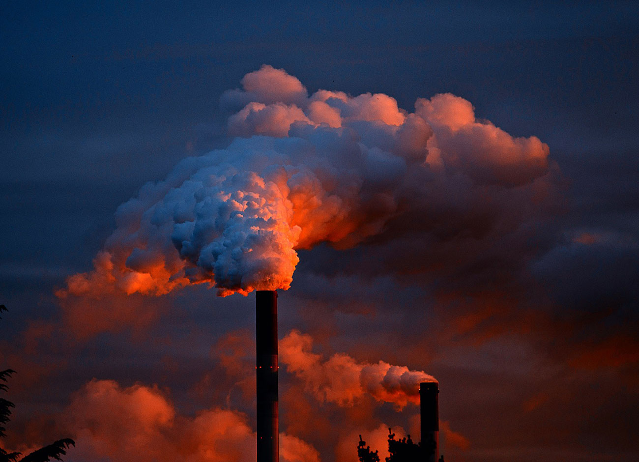 Smoke billows out of a factory at sunset.