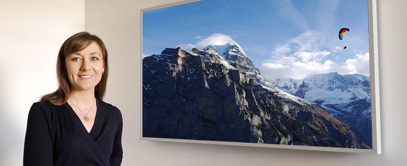 a woman stands in front of a framed television that appears to be a framed image of a paraglider