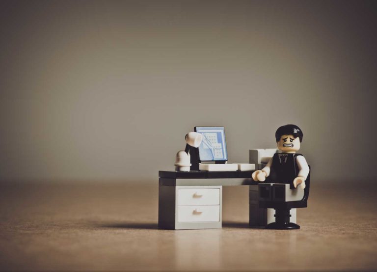 a photo illustration of a LEGO man sitting at a desk looking stressed