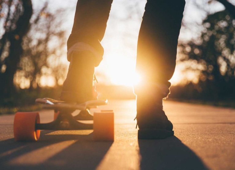 close up image of a teens feet on a skateboard riding into the sunset