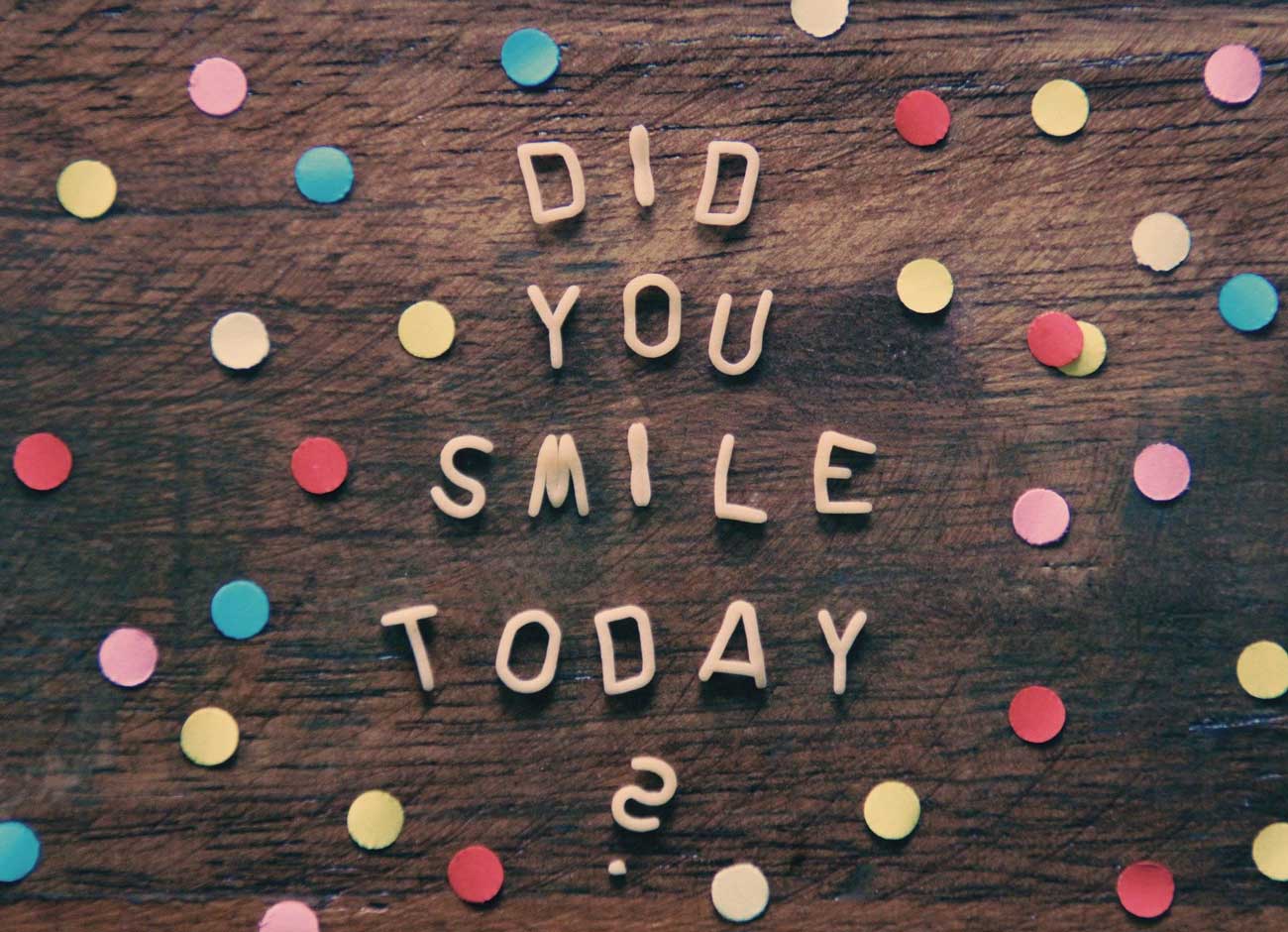 a table with a question written wooden letters Did you smile today? surrounded by confetti