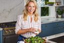 a blonde woman makes a salad in a sunny kitchen