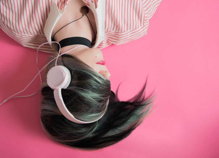 a teenage girl wears headphones with her hair swooped across her eyes. It is hard to tell how she is feeling.