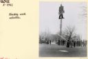 A black and white image from 1942 of a wooden Paul Bunyan statue atop a ladder. A group of men is using a firehose to keep people away while they figure out how to get Bunyan down.