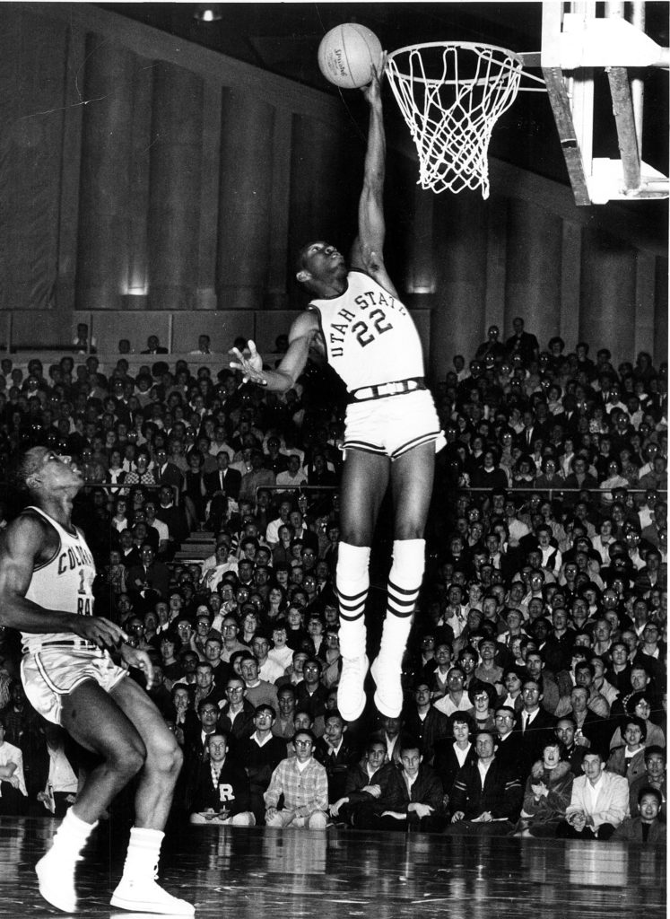 An African American basketball player wearing the 22 uniform is captured mid-air holding a basketball. His hand grazes the rim. 