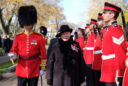 a woman dressed in a black coat and hat stands between guardsmen clad in red uniforms during a Canadian ceremony.