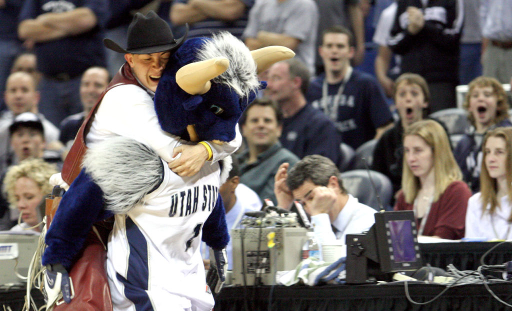 a cowboy mascot jumps on the back of Utah State mascot Big Blue during a fight at a basketball game.