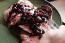 a plate of elk meat with a scoop of blueberry sauce being spooned over the top.