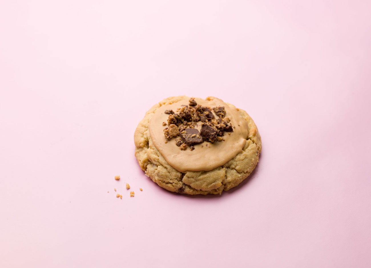 a tempting sugar cookie with a peanut butter frosting and topping with crumbled peanut butter cups rests on a pale pink piece of paper.