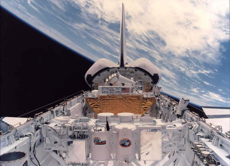 an image from space where Earth is visible in the background and the camera is trained on the back of the space shuttle