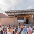 Red rock cliffs flank USU's first net-zero building. Hundreds of people gather out front for the ribbon cutting ceremony.