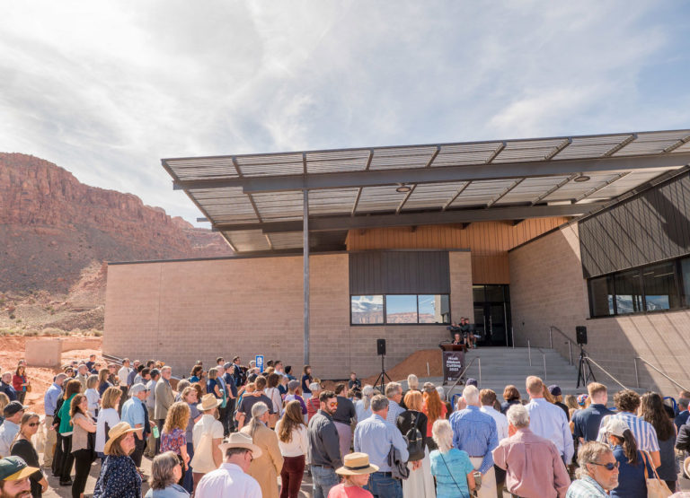 Red rock cliffs flank USU's first net-zero building. Hundreds of people gather out front for the ribbon cutting ceremony.