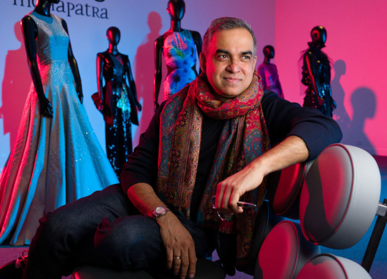 Bibhu Mohapatra sits on a chair. Behind him are dresses of his design.