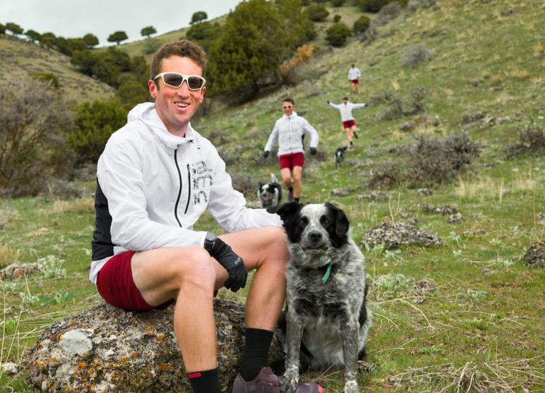 Ultrarunner Michael McKnight with white sunglasses sits on a rock with his dog. Behind him are images of the same man running behind him to give the effect of motion