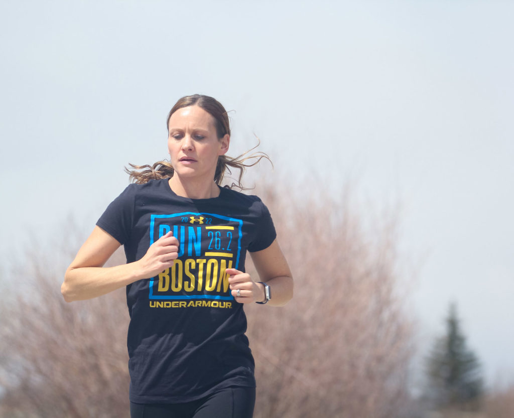 a woman in a boston marathon t-shirt is running with a determined look