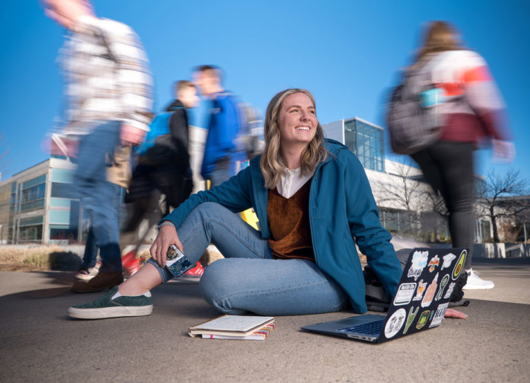 a student sits with her laptop open as a blur of students walk by her