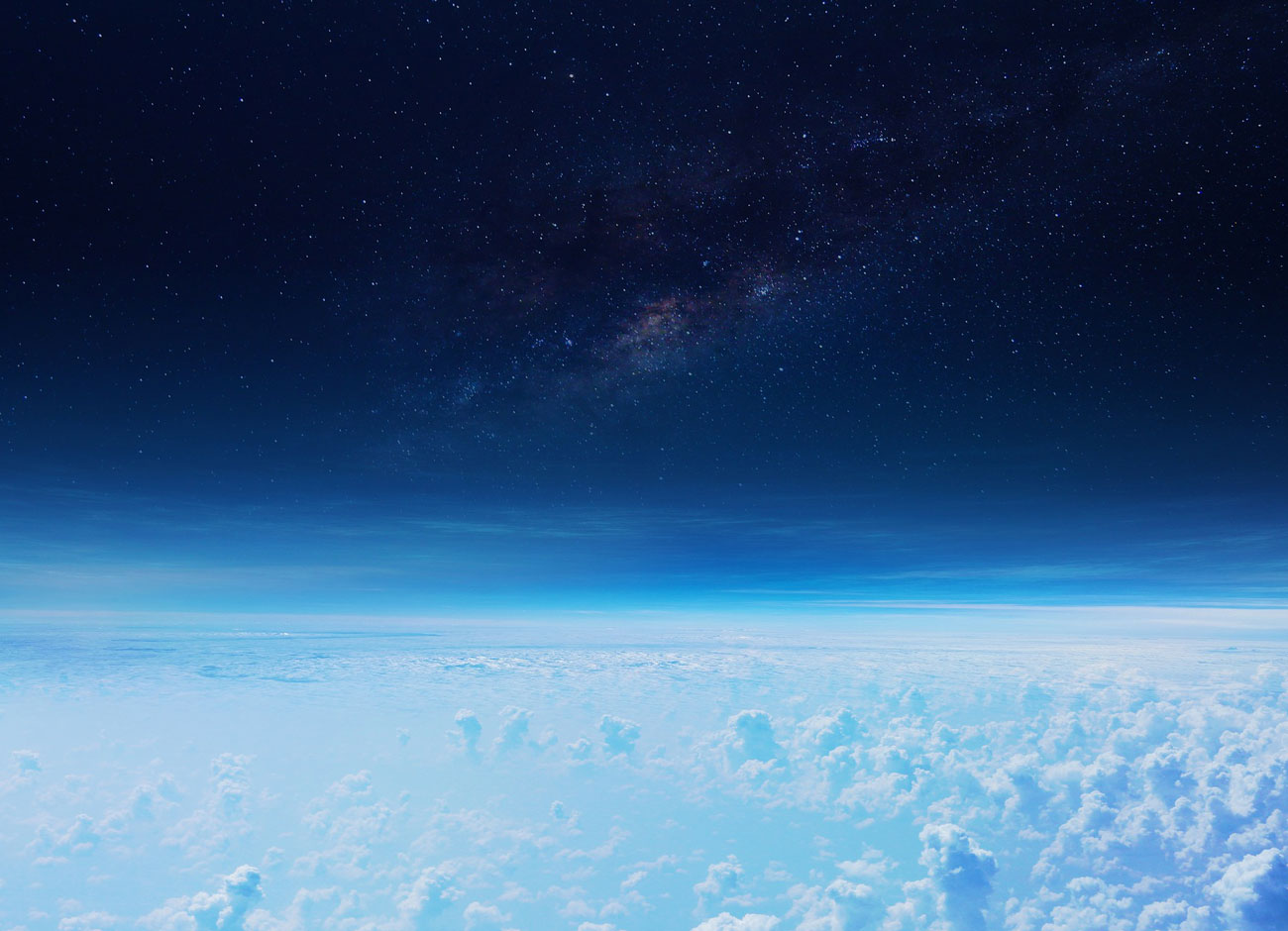 a view of the stratosphere from space. Clouds below, a hazy blue line and then the darkness of space with stars.