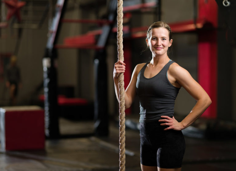 an athletic young woman in workout gear holds onto a large rope at a Ninja Warrior gym