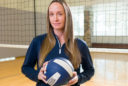 Former volleyball player Amy Crosbie works on equity issues in women's sports these days. She poses in the gym with a volleyball and net.