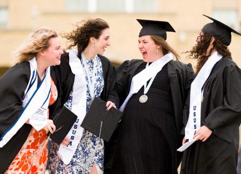 Four female students celebrate in their caps and gowns during USU's 2023 commencement ceremonies.