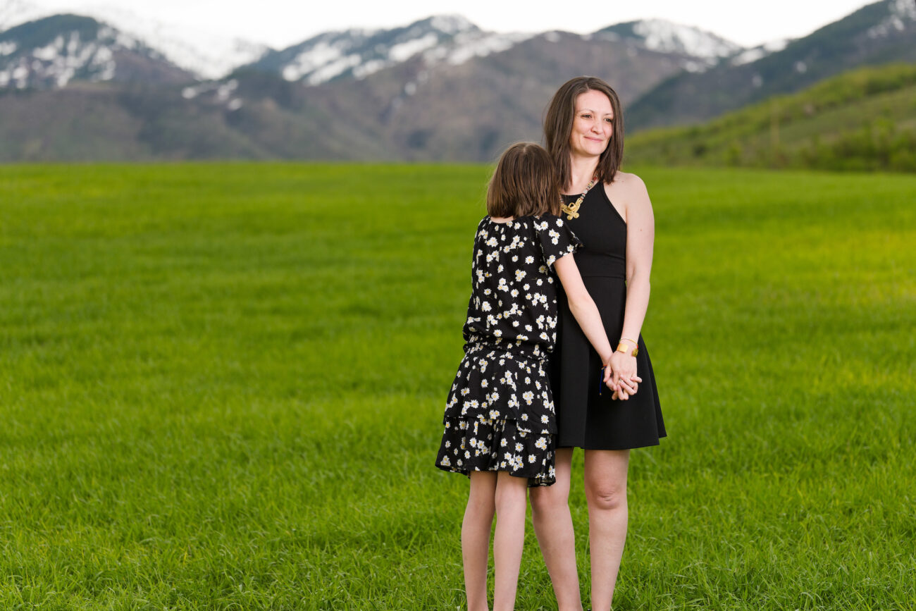 USU doctoral candidate Claudia Wright stands with her daughter in a green field with snowcapped mountains in the background.