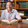 USU history professor Seth Archer poses in the library with an open book in front of him for a photo.