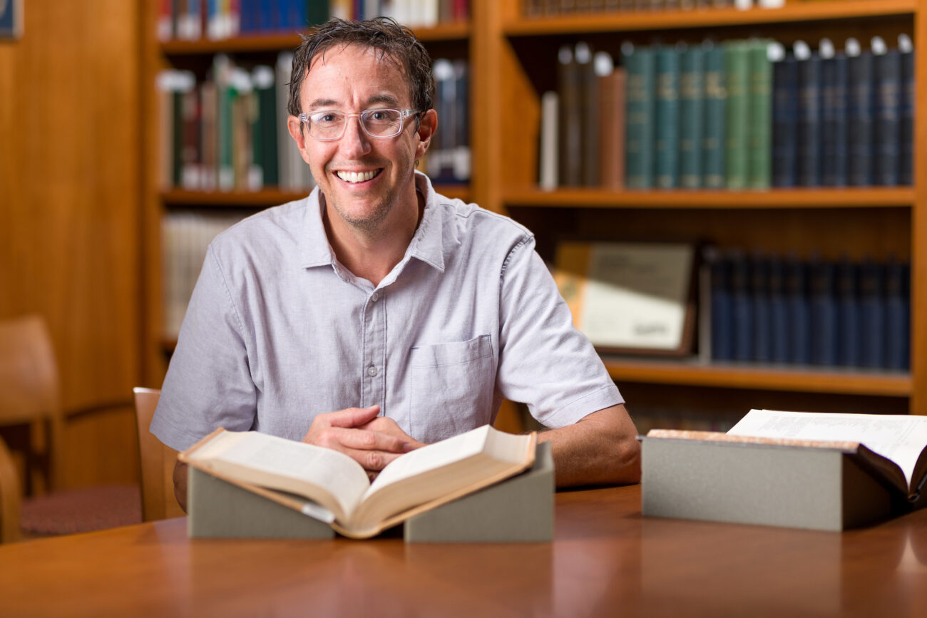 USU history professor Seth Archer poses in the library with an open book in front of him for a photo.