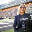 New USU athletic director Diana Sabou poses for a picture in the north end zone of Maverik Stadium, with USU's West Stadium Complex and press box rising behind her in the background.
