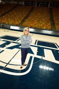 New USU athletic director Diana Sabou stands at center court of the Dee Glen Smith Spectrum on top of the Aggies' U-State logo.