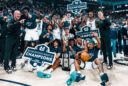 The 2023-24 USU men's basketball team poses on the court with signs and t-shirts as they celebrate winning the regular season Mountain West conference championship.