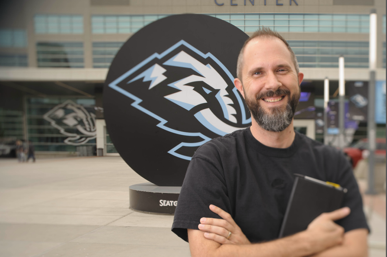 A man stands in front of an arena featuring the Utah Mammoth logo he designed.