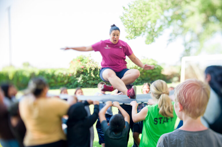 A group of teenagers bounces a woman on a trampoline.