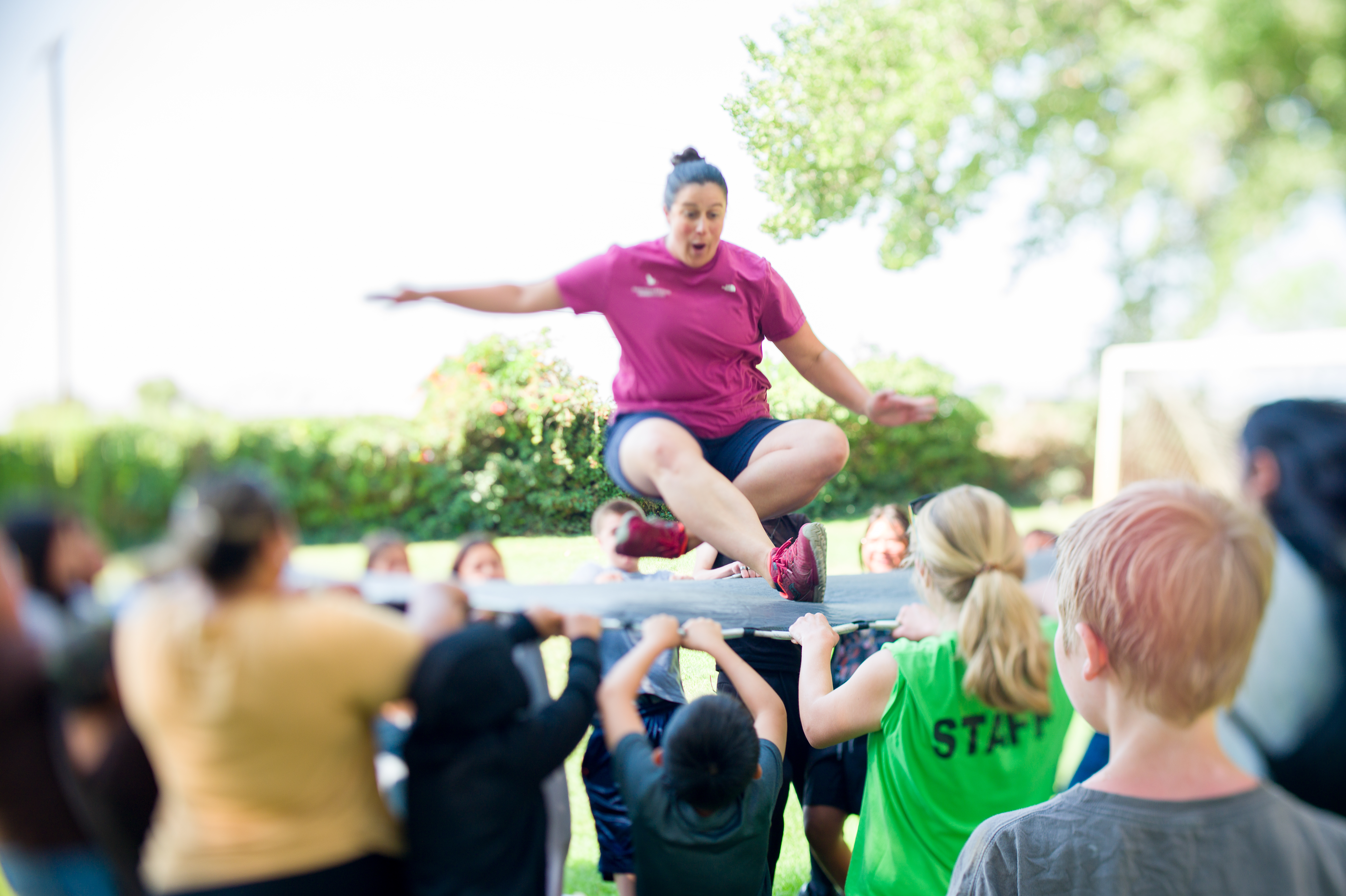 A group of teenagers bounces a woman on a trampoline.