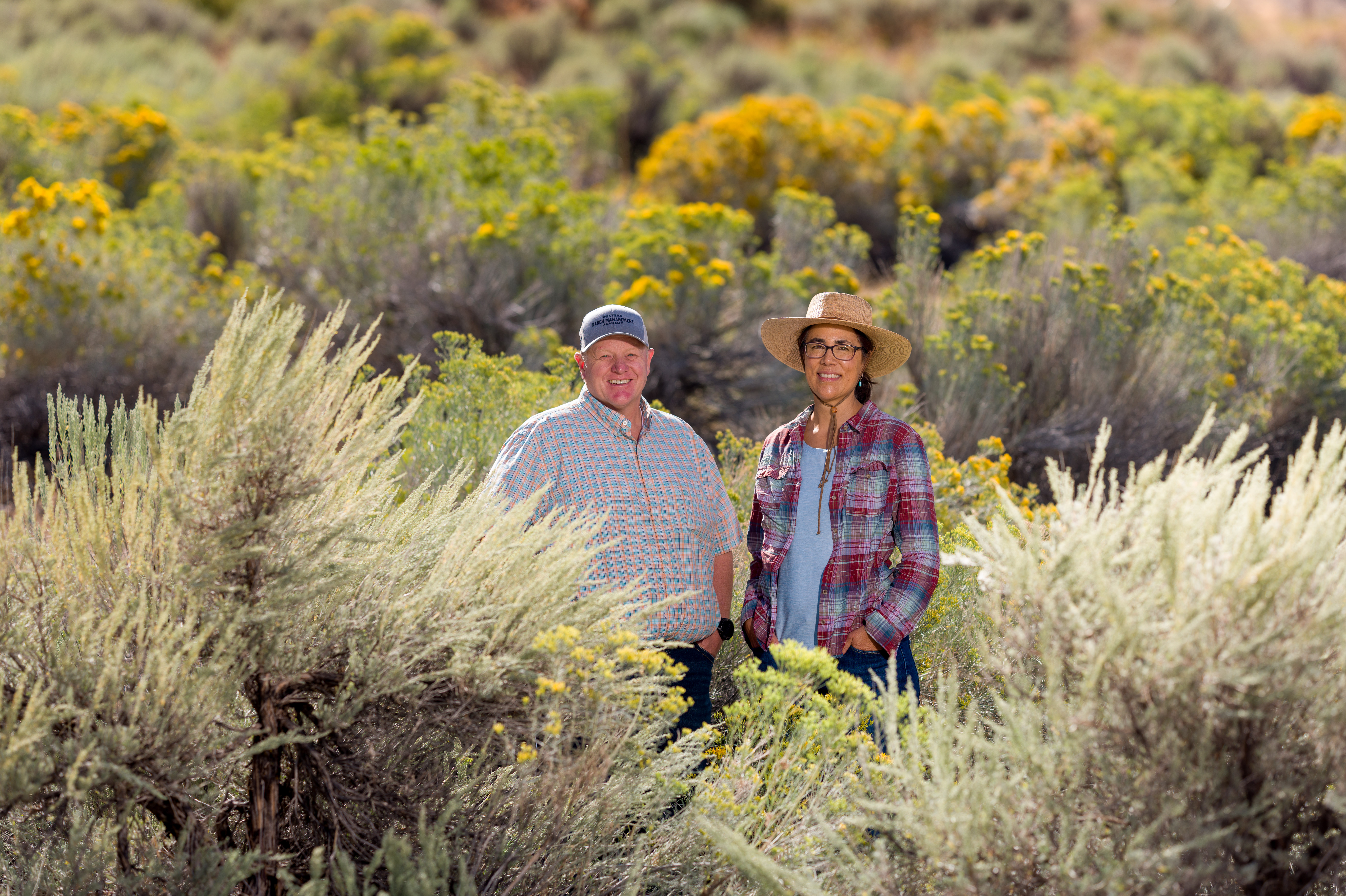 A man and woman, USU Extension workers, stand amidst sagebrush.
