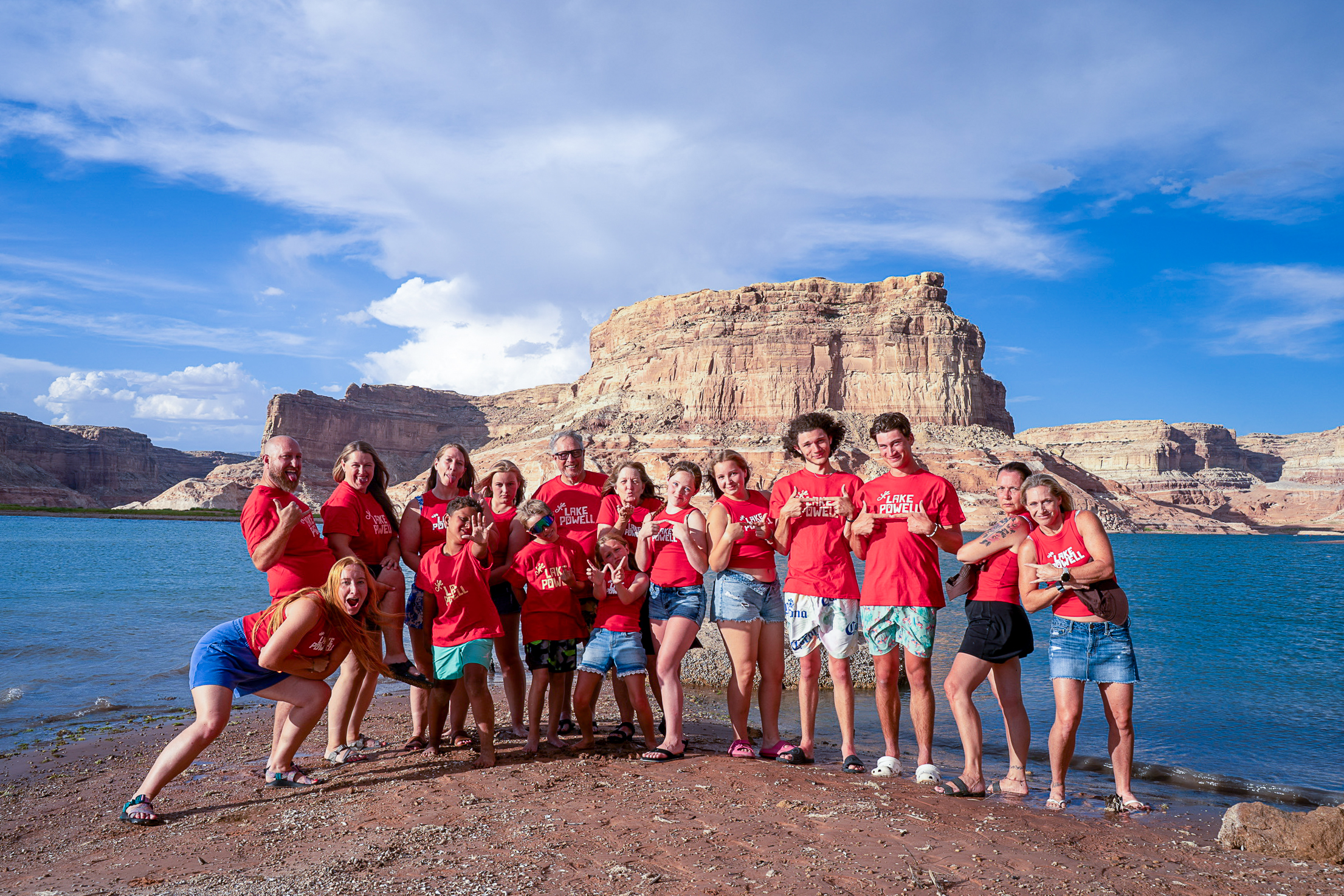 Utah State managing editor Tim Olsen and his family pose for a photo on the beach at Lake Powell with water and a sandstone mesa behind them.