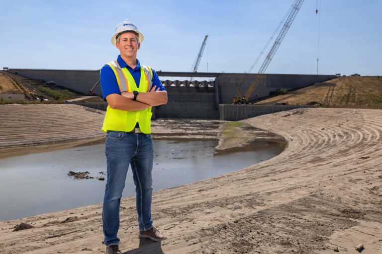 A man in a hard hat and reflective vest stands in front of a dam he engineered in north Texas.